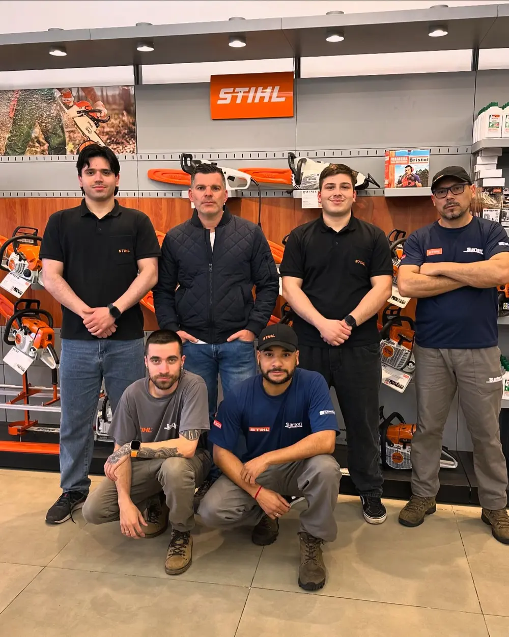 A equipe da Sartori Máquinas em frente à parede de motosserras STIHL