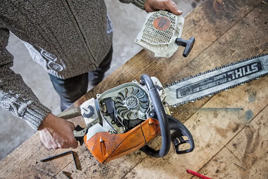 Motosserra STIHL aberta na bancada da oficina, com o conjunto de partida ao lado